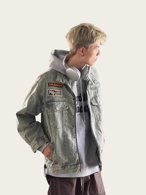 Person wearing a gray denim jacket with patches on a light background