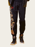 Black pants with floral embroidery and a red emblem worn by a person on a beige background