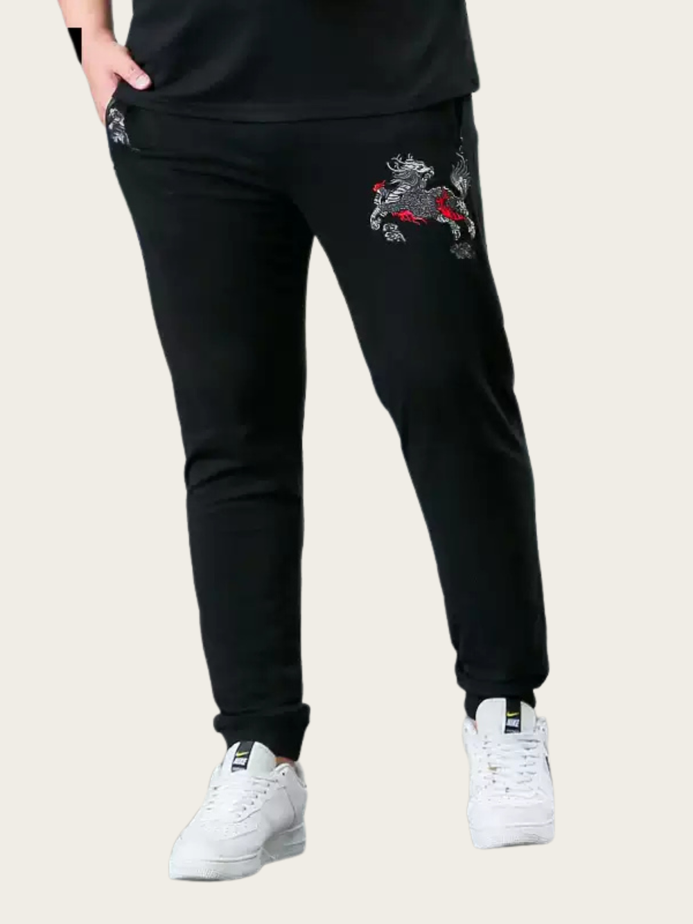 Black jogger pants with embroidered designs on a beige background