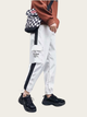 Person wearing white cargo pants with black accents and a checkered bag on a light gray background