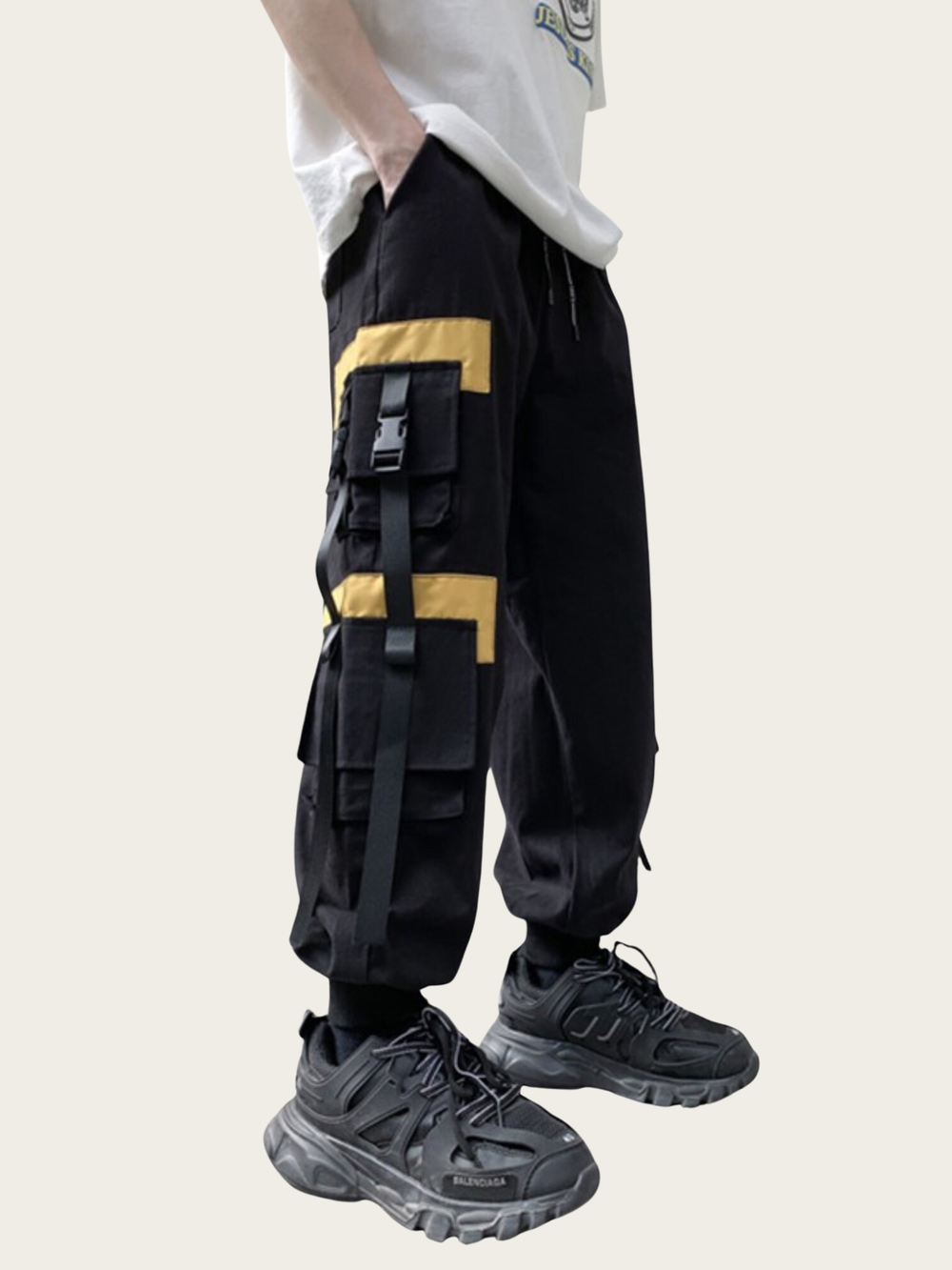 Person wearing black cargo pants with yellow accents and black shoes on a white background