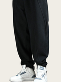 Black jogger pants worn with white sneakers on a beige background