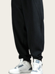 Black jogger pants worn with white sneakers on a beige background