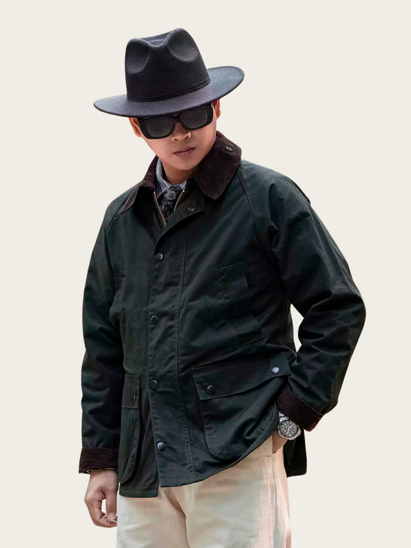Person wearing a dark green jacket, black hat, and sunglasses on a plain background