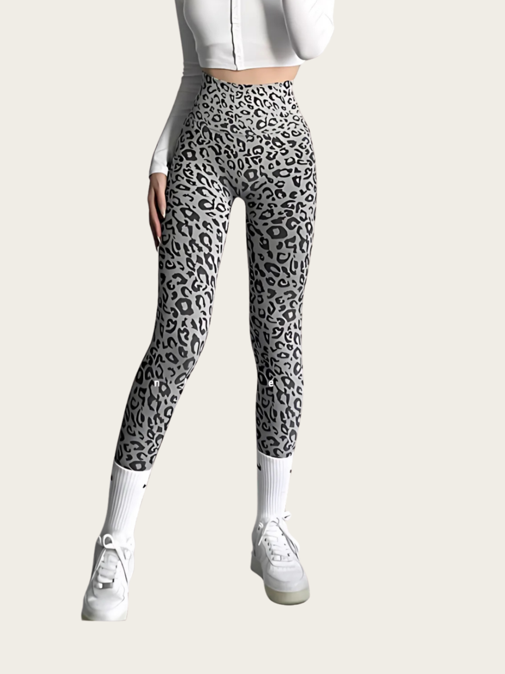 Person wearing leopard print leggings with a white top and shoes on a light gray background