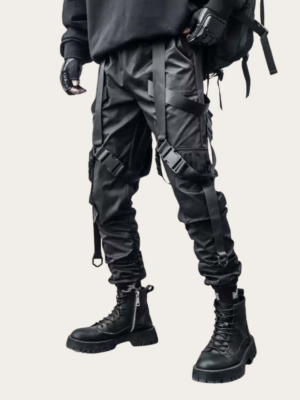 Person wearing black tactical pants with multiple straps and a backpack on a beige background