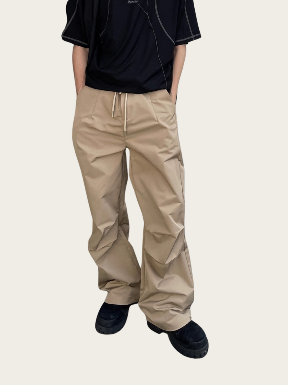 Person wearing beige pants and black shoes on a plain background