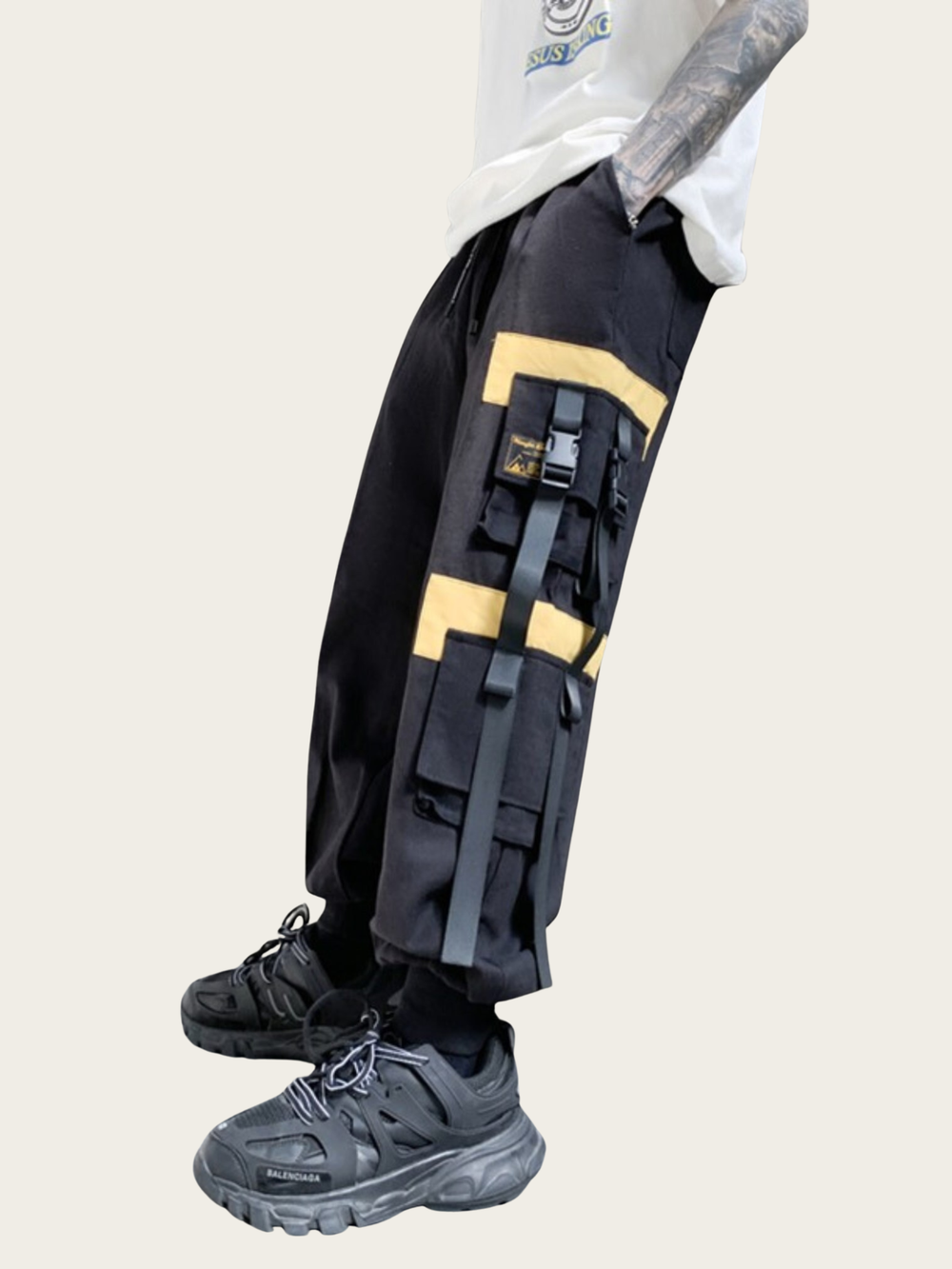 Person wearing black tactical pants with yellow accents on a light gray background