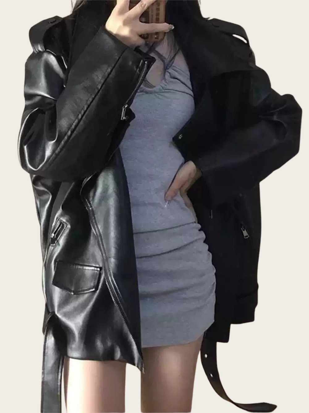 Person wearing a black leather coat over a gray dress on a plain background
