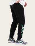 Black jogger pants with green design worn by a person on a white background