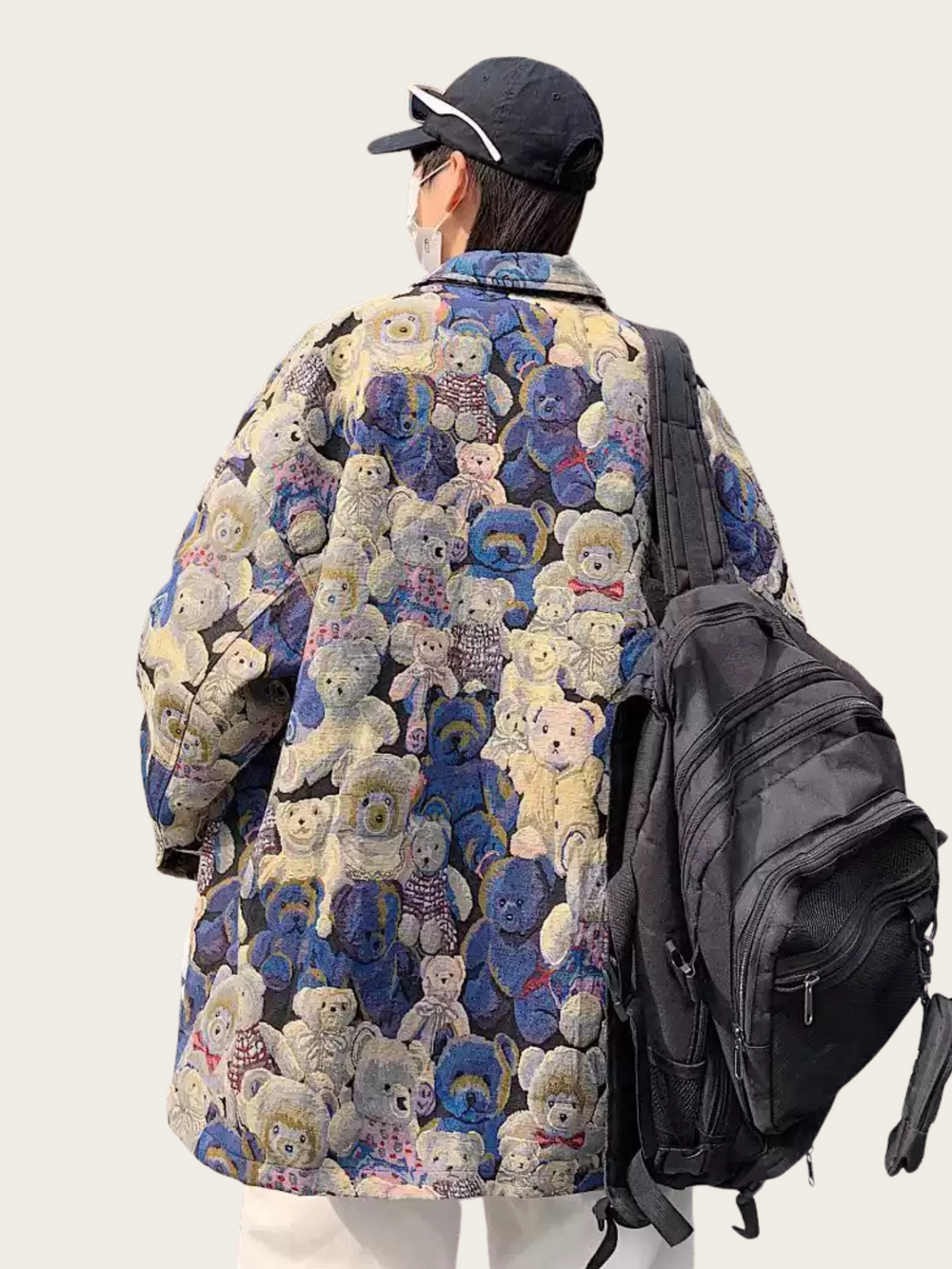 Person wearing a colorful teddy bear patterned coat with a black backpack on a white background