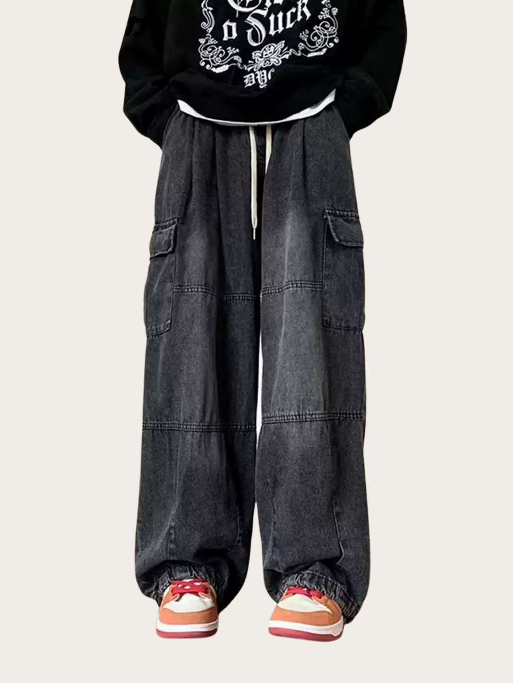 Person wearing a black hoodie with white text and dark gray baggy pants on a light beige background
