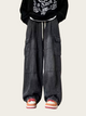 Person wearing a black hoodie with white text and dark gray baggy pants on a light beige background