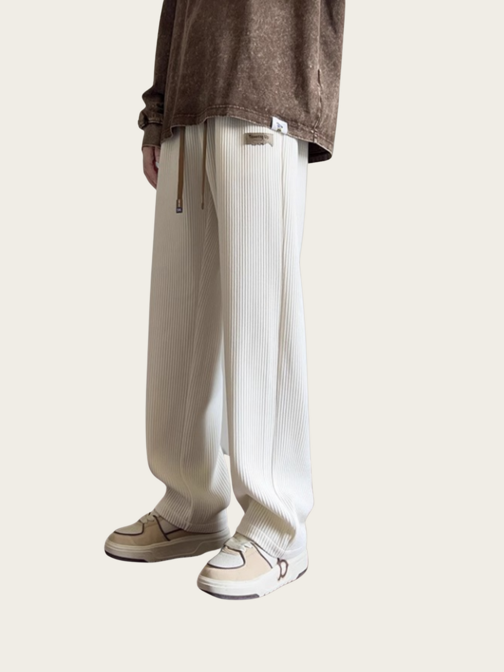 Person wearing white ribbed pants and a brown top on a light beige background