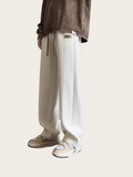 Person wearing white ribbed pants and a brown top on a light beige background