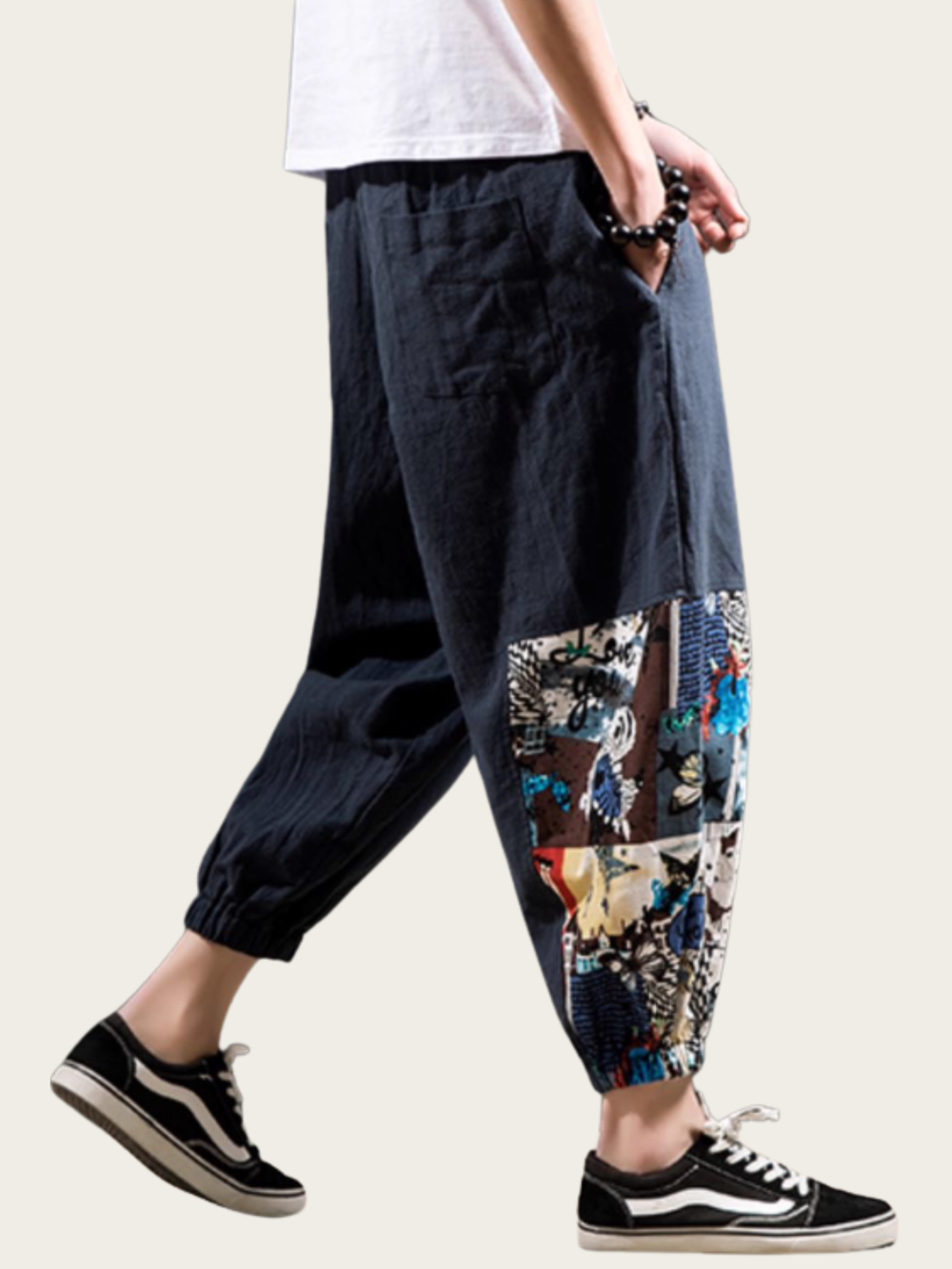 Person wearing dark blue pants with floral patterned cuffs and white sneakers on a light background