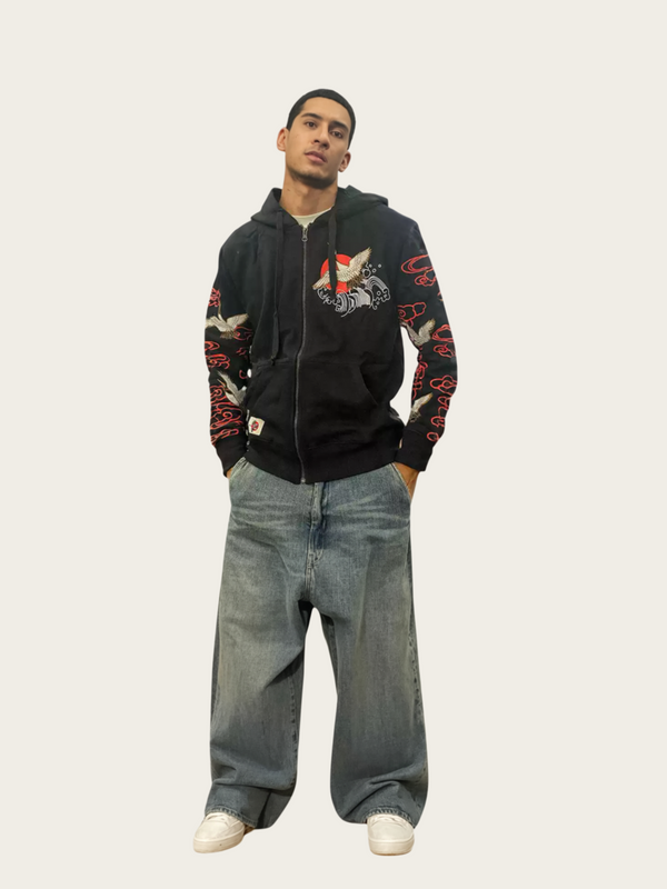 Person wearing a black hoodie with colorful designs and blue jeans on a white background