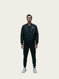Person wearing a black bomber jacket with branding on a light gray background