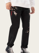 Black pants with floral embroidery worn by a person on a white background