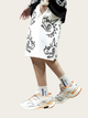 Person wearing a white skirt with black graphics and white sneakers with orange accents on a light background