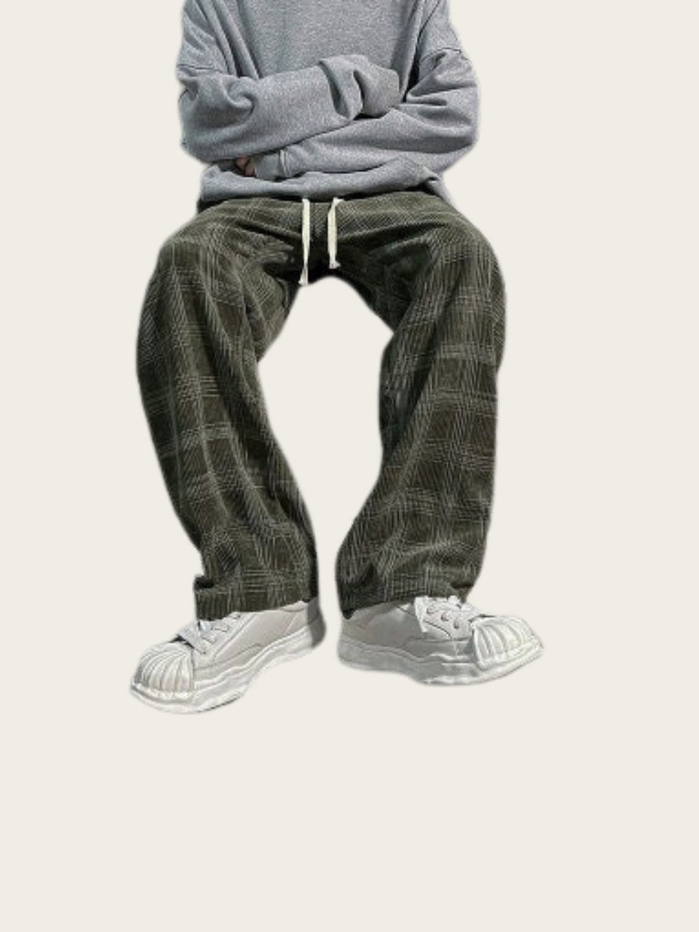 Person wearing gray sweatshirt and plaid pants with white sneakers on a light gray background