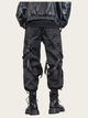 Person wearing black tactical pants with multiple pockets and straps on a beige background