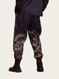 Person wearing black pants with intricate gold and red patterns on a beige background