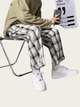 Person sitting on a chair wearing plaid pants and white sneakers, holding a phone.