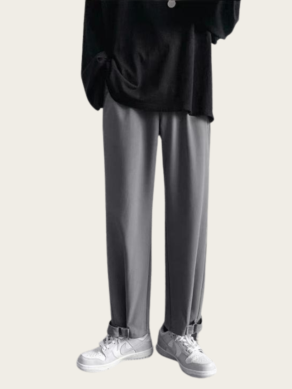 Person wearing black top and gray pants with white sneakers on a light gray background