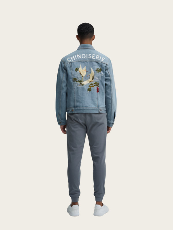 Person wearing a blue denim jacket with 'Chinoiserie' text and bird design on the back, standing against a white background.