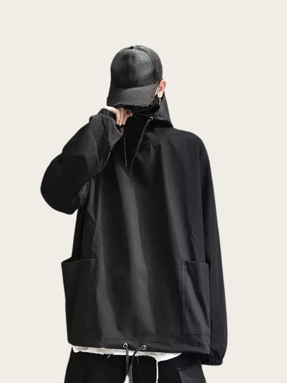 Person wearing a black jacket and cap on a light beige background