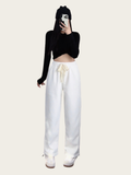 Person wearing a black long-sleeve crop top and white pants on a plain background