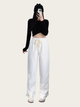Person wearing a black long-sleeve crop top and white pants on a plain background