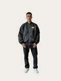 Person wearing a dark jacket with a logo on a plain background