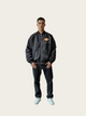 Person wearing a dark jacket with a logo on a plain background