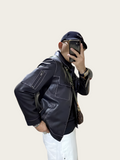 Person wearing a black leather jacket and white pants, taking a mirror selfie.