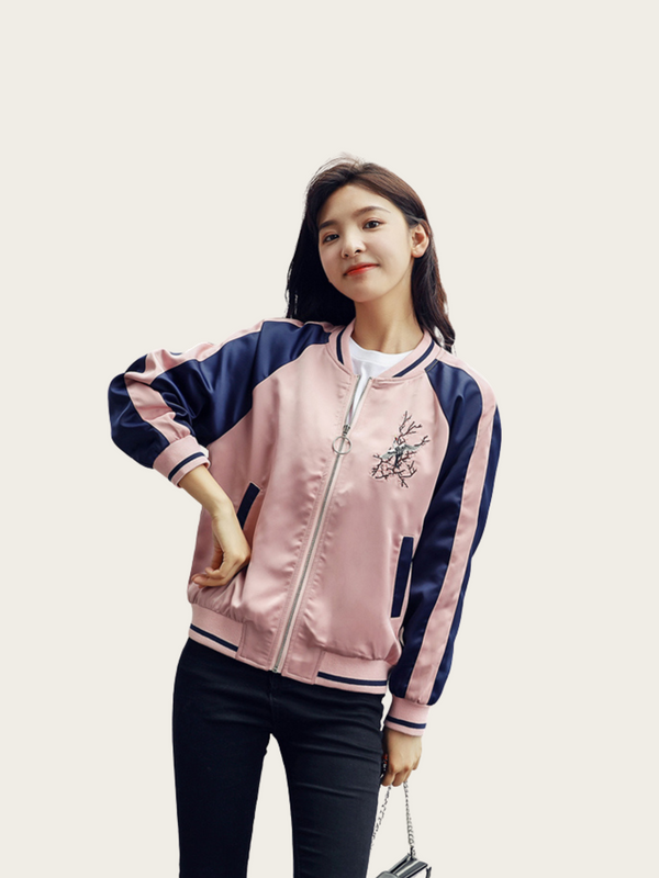 Woman wearing a pink and navy bomber jacket with a floral design on a plain background