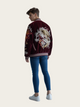 Person wearing a burgundy bomber jacket with floral embroidery on a plain background