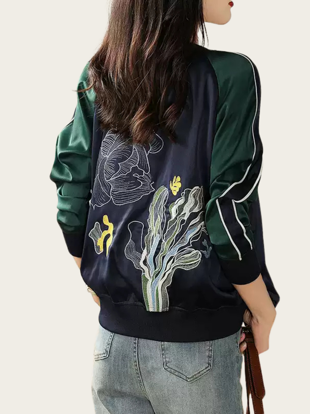 Person wearing a dark green bomber jacket with floral embroidery on a light background