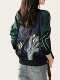 Person wearing a dark green bomber jacket with floral embroidery on a light background