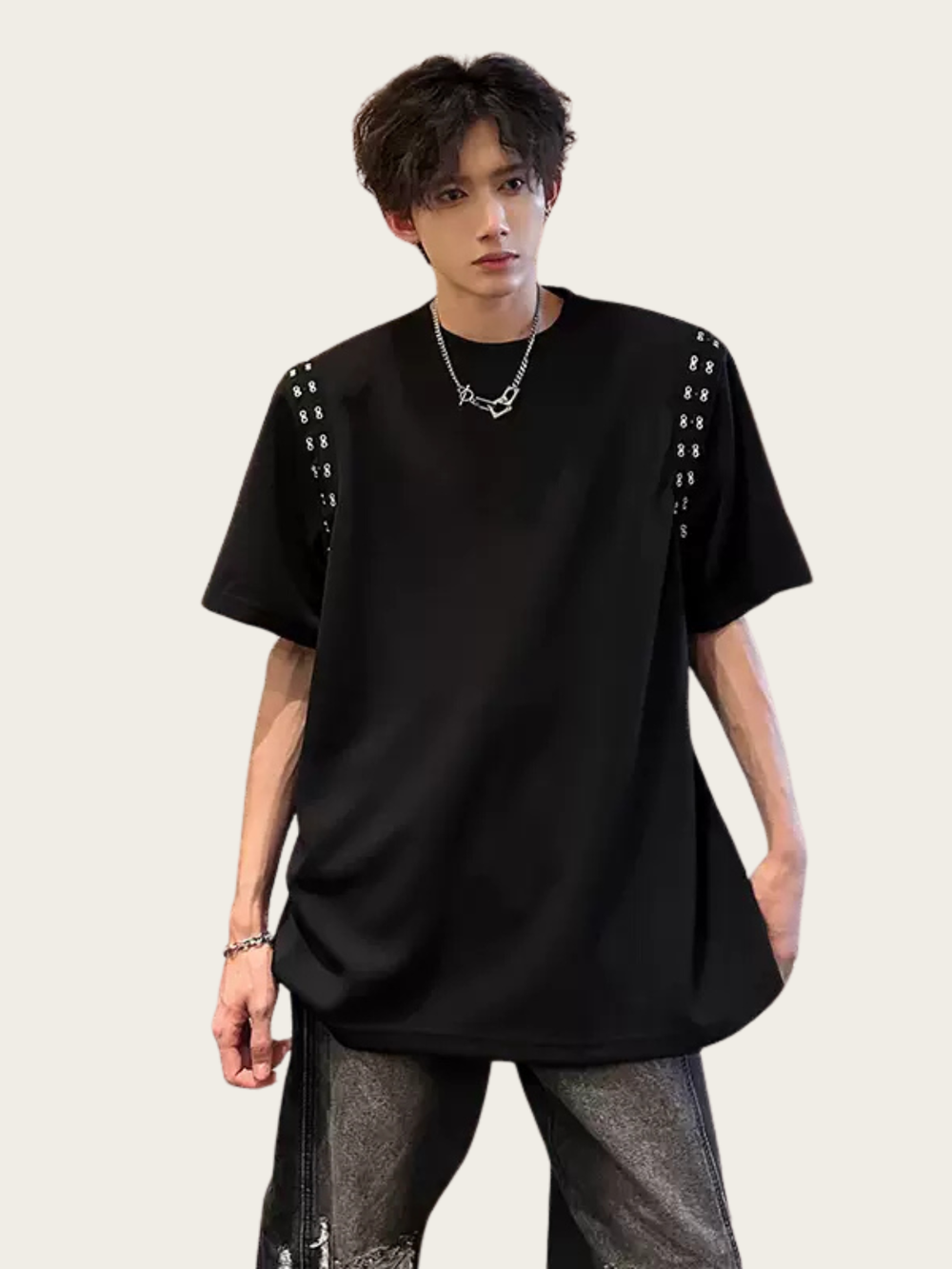 Person wearing a black oversized t-shirt with studded details on a plain background