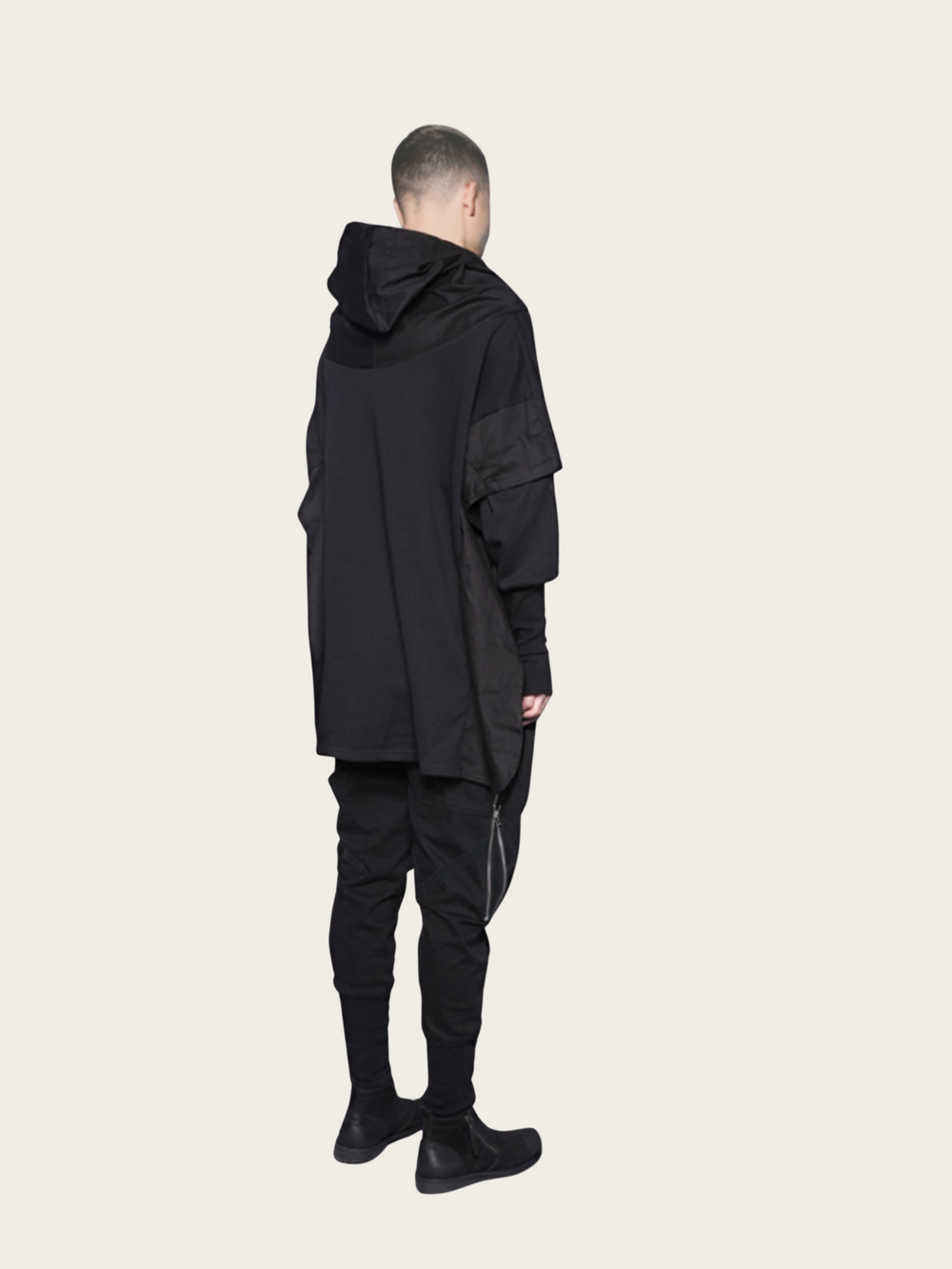 Person wearing a black hooded outfit on a beige background