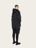 Person wearing a black hooded outfit on a beige background