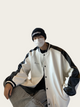 Person wearing a white and black varsity jacket with a plain background