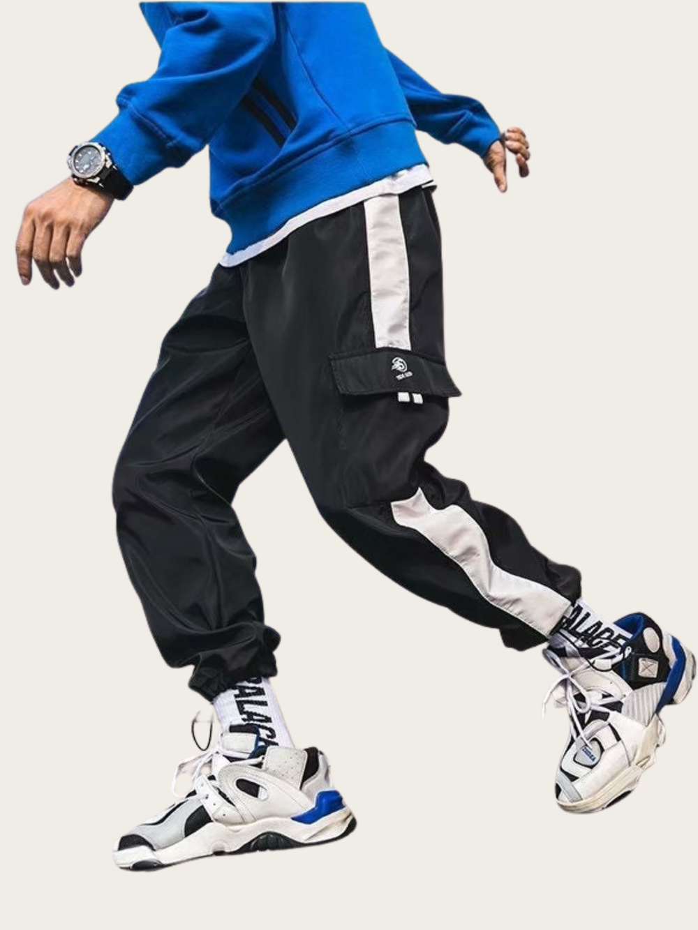 Person wearing a blue sweatshirt, black and white pants, and white sneakers on a light gray background