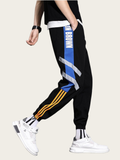 Black jogger pants with colorful stripes worn by a person on a beige background