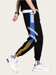 Black jogger pants with colorful stripes worn by a person on a beige background