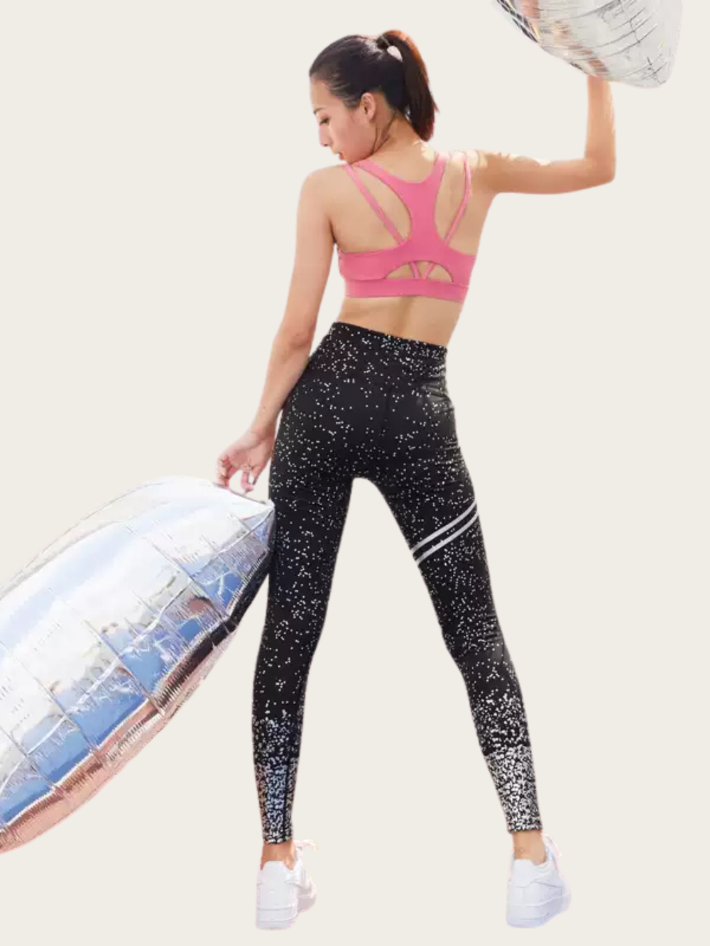 Woman wearing a pink sports bra and black leggings with white speckles, holding an inflatable ring.