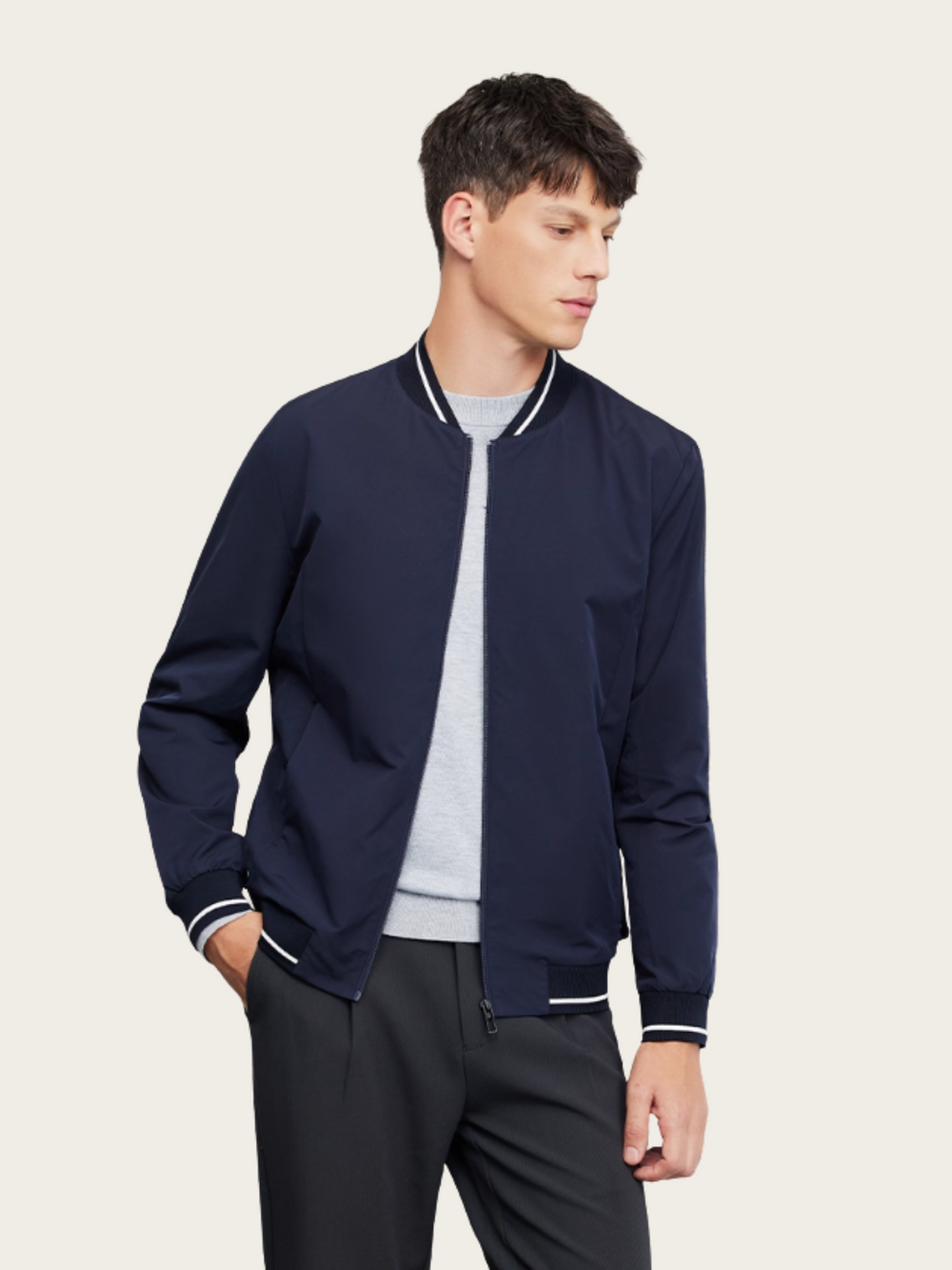 Man wearing a navy bomber jacket over a gray shirt on a beige background