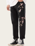Black pants with floral embroidery worn by a person on a white background